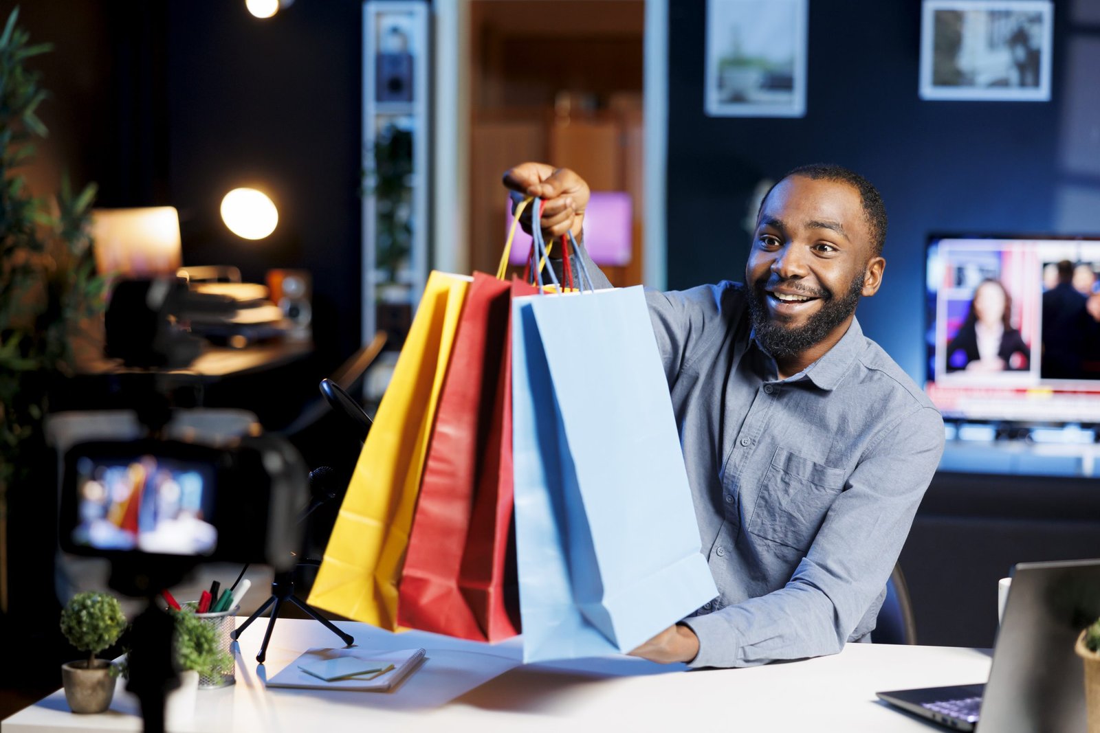 African american man holding shopping bags in hand, showing subscribers purchases he recently got. Content creator presenting viewers new acquisitions, filming himself at home